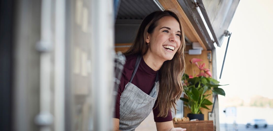 Eine lachende Frau schaut aus einem Food-Truck