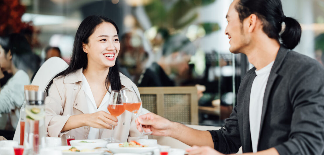 Eine Frau und ein Mann sitzen in einem Restaurant und stoßen an.