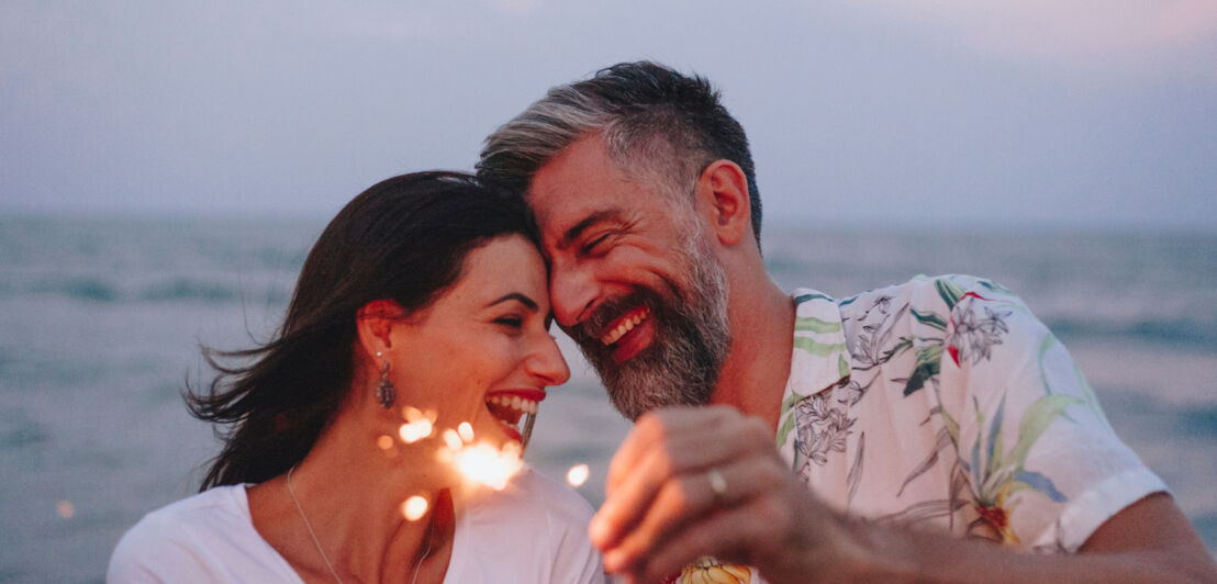 Eine Frau und ein Mann mit Wunderkerzen in der Hand am Strand