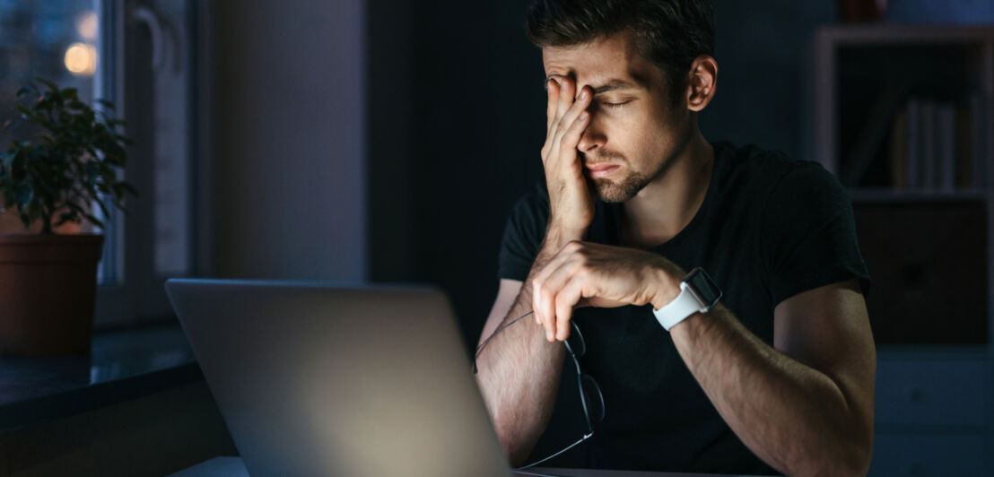 Ein Mann sitzt vor einem Laptop und reibt sich die Augen.