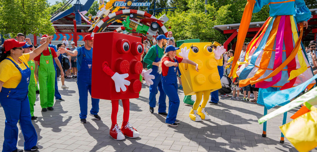 Legosteine mit Beinen und Menschen in Latzhosen machen eine Parade