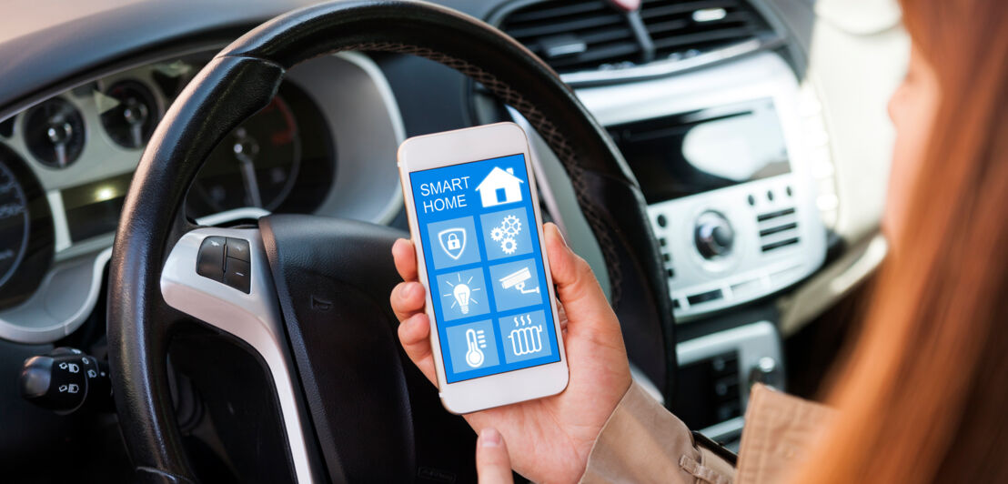 Frau im Auto blick auf ihr Handy und kontrolliert ihr Smarthome