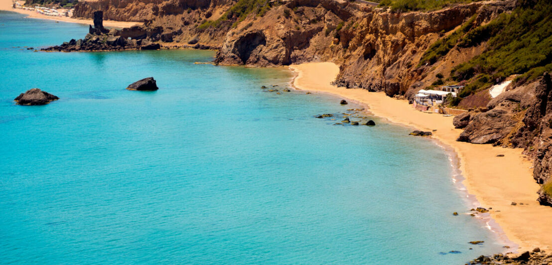 Eine kleine, felsige Bucht mit Sandstrand und Strandkiosk am türkisblauen Meer