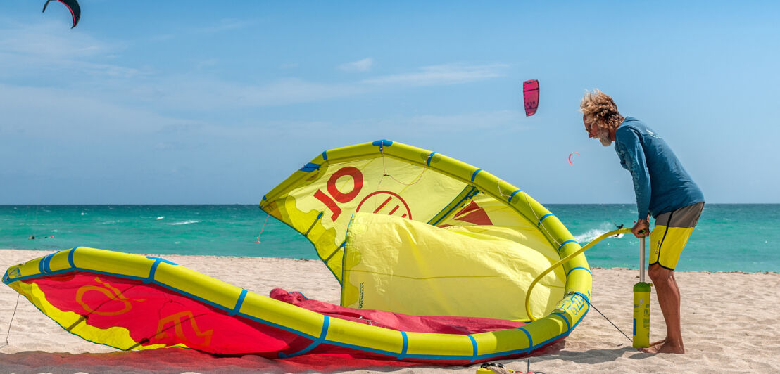 Kitesurfer pumpt am Strand sein Kite mit einer Pumpe auf