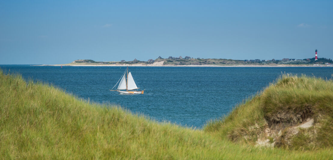 Blick durch die Dünenlandschaft aufs Meer, auf dem ein Segelboot fährt