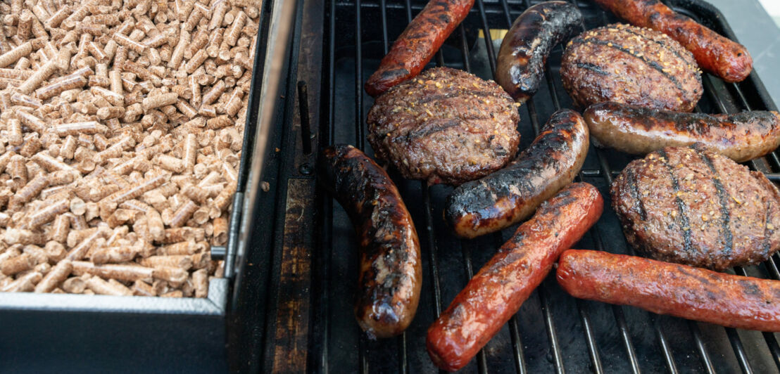 Bratwurst und Buletten auf einem Rost neben einer Schale mit Pellets