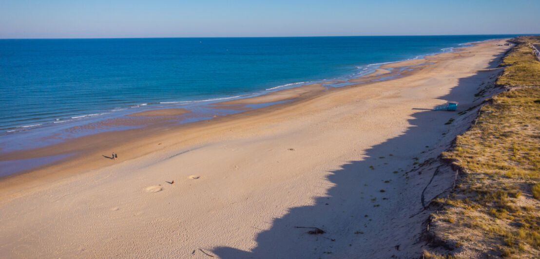 Ein langer Strand am Meer, dahinter Dünen