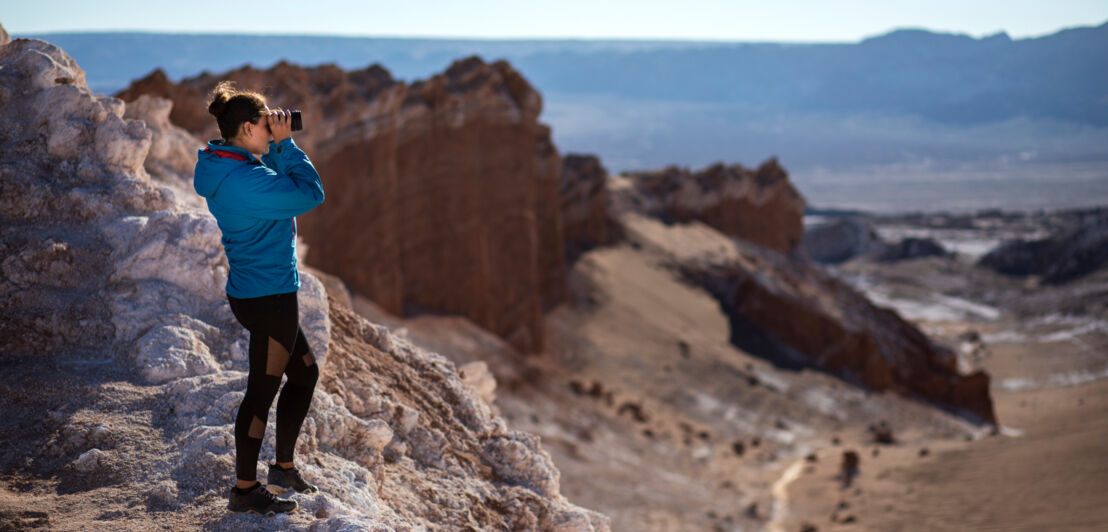 Eine junge Frau mit Fernglas steht auf einem Felsen