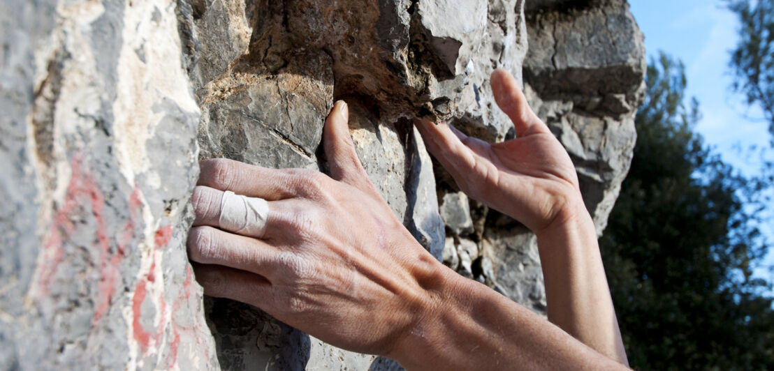 Die Hände eines Kletternden halten sich an einer Steinwand fest