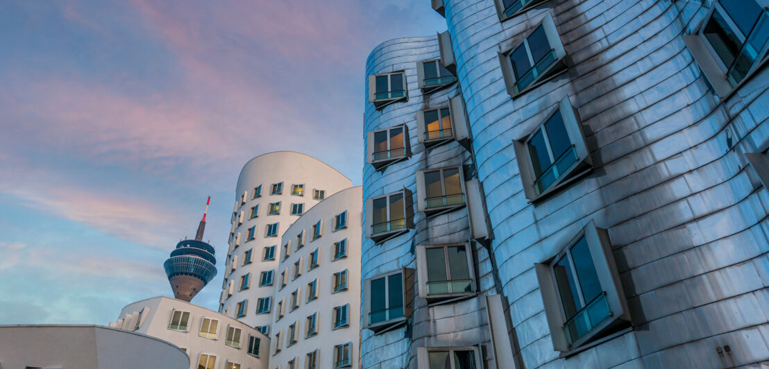 Geschwungene, moderne Gebäude in Düsseldorf mit Fernsehturm im Hintergrund