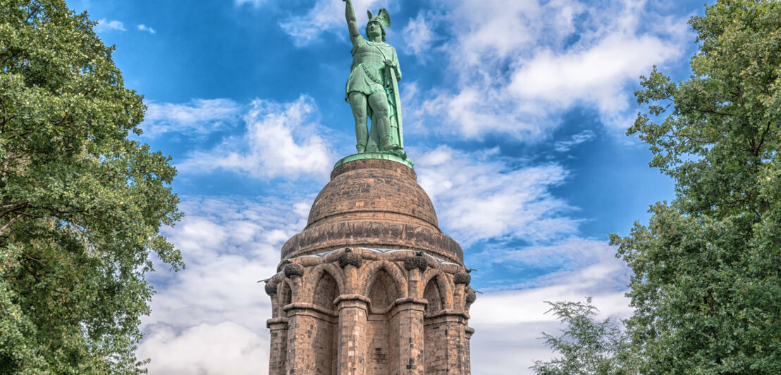 Ein Denkmal zwischen Bäumen und vor blauem Himmel