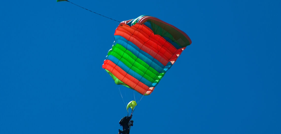 Ein bunter Fallschirm mit zwei Springern.