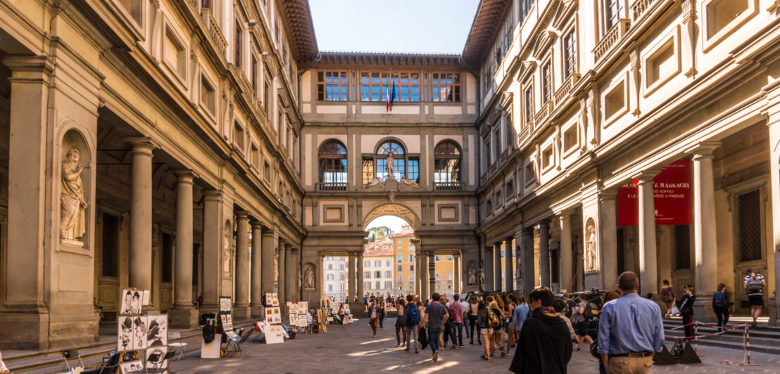 Menschen gehen durch eine historische Gasse mit Kunstschaffenden am Rand