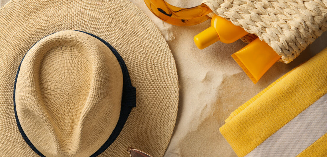 Stillleben mit Strohhut und Sommer-Accessoires im Sand