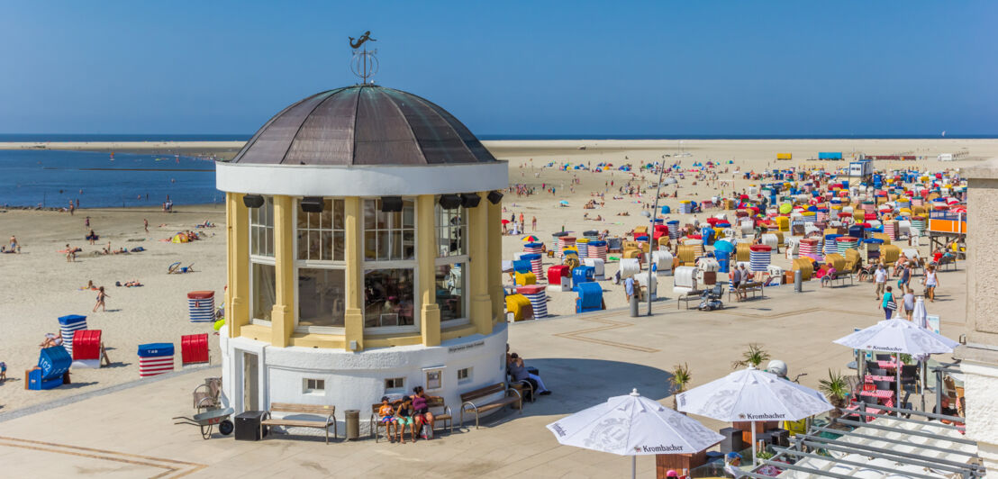 Eine Promenade mit Musikpavillon an einem Sandstrand mit bunten Strandkörben