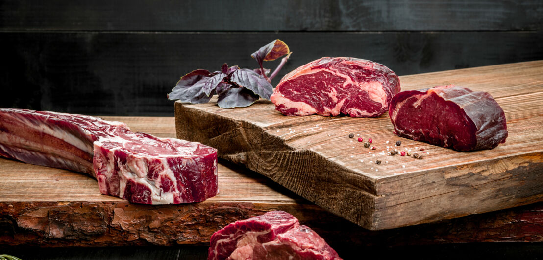 Rohes Rindfleisch auf Schneidebrett mit Gewürzen, frischem Basilikum und einem Zweig Rosmarin auf Holzgrund