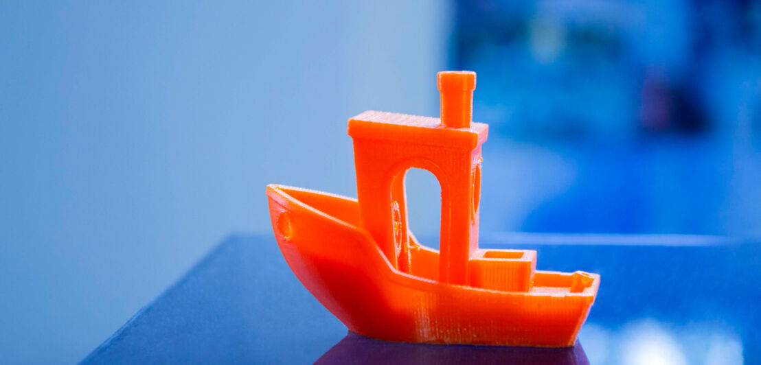 Ein kleines, mit einem 3D-Drucker erstelltes Modellboot aus orangenem Plastik 