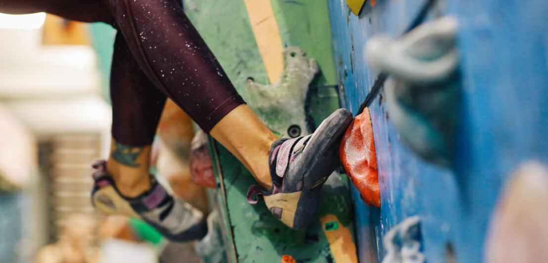 Nahaufnahme von Füßen mit Kletterschuhen an einer Kletterwand