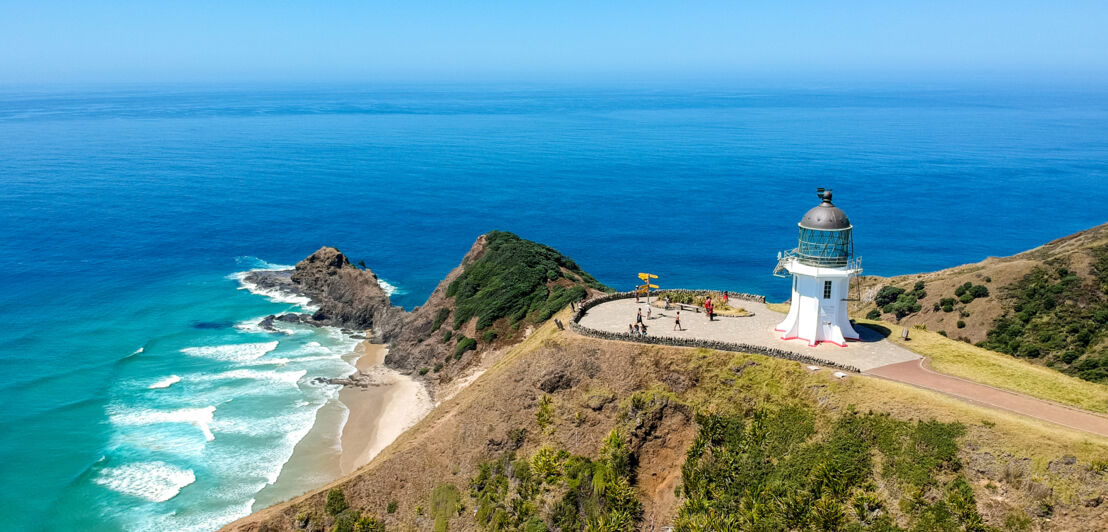 Blick von oben auf einen kleinen Leuchtturm, der nahe einer Klippe steht