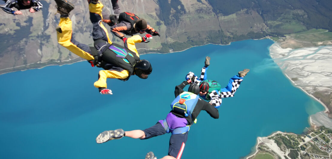 Mehrere Menschen beim Fallschirmspringen oberhalb eines Sees.