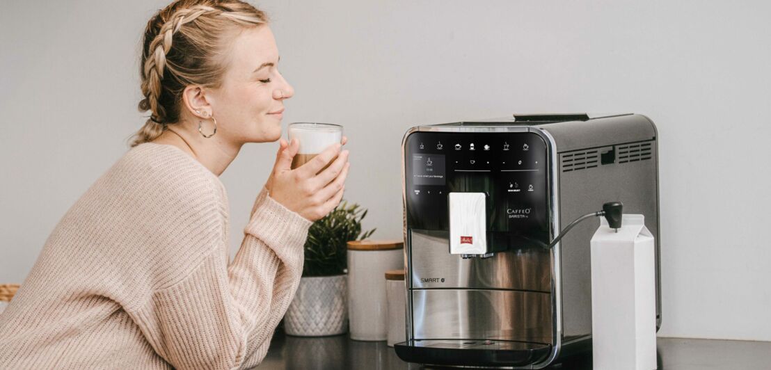 Eine Frau sitzt vor einer Kaffeemaschine und genießt ihren Kaffee