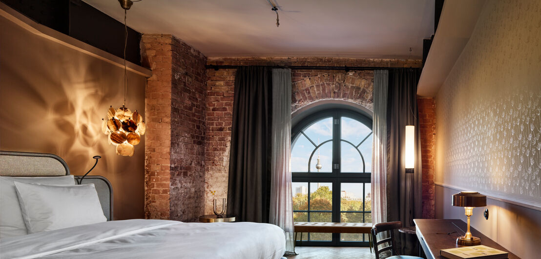 Modernes Hotelzimmer mit Backsteinwand und Fensterbogen mit Blick auf den Berliner Fernsehturm