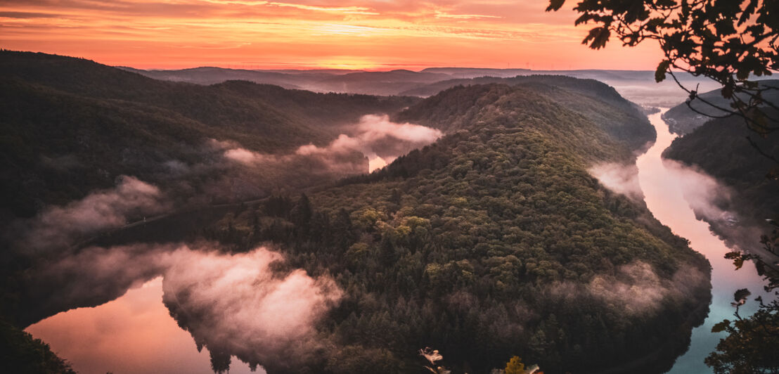 Sonnenaufgang über einem hügeligen Gebiet, durch das sich ein Fluss zieht