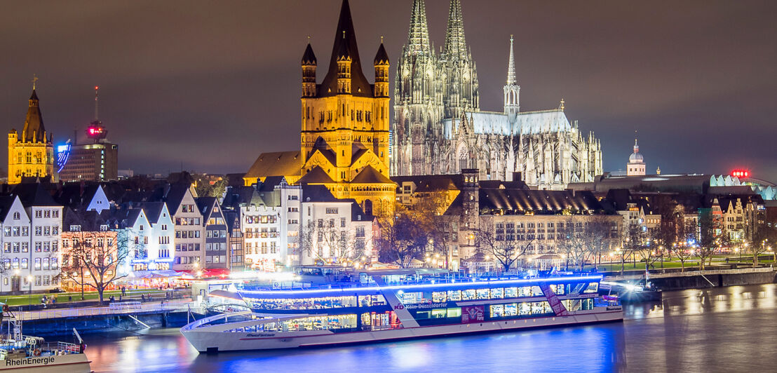 Beleuchtetes Schiff auf dem Rhein vor dem Kölner Dom. 