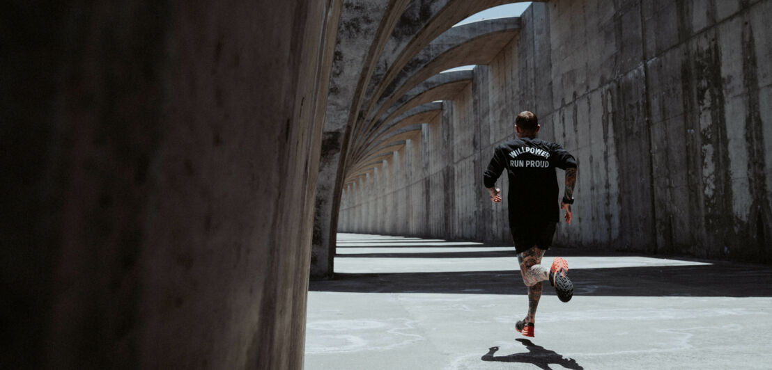 Eine Person in der Rückansicht joggt durch Arkaden