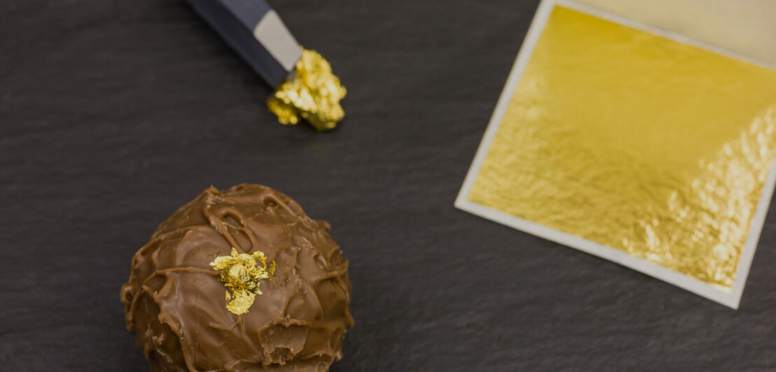 Hauchdünnes Blattgold auf einer Praline, daneben Blattgold in einer Verpackung