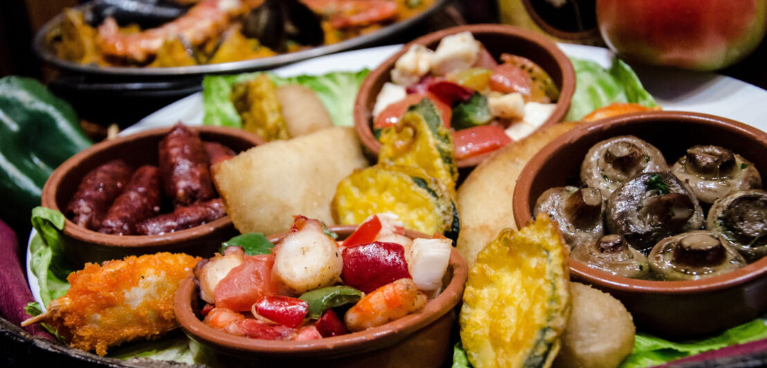 Tablett mit mehreren Schälchen Tapas wie Pilzen, Wurst und Gemüse