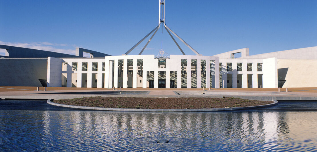 Modernes weißes Parlamentsgebäude vor einer Wasserfläche in Canberra