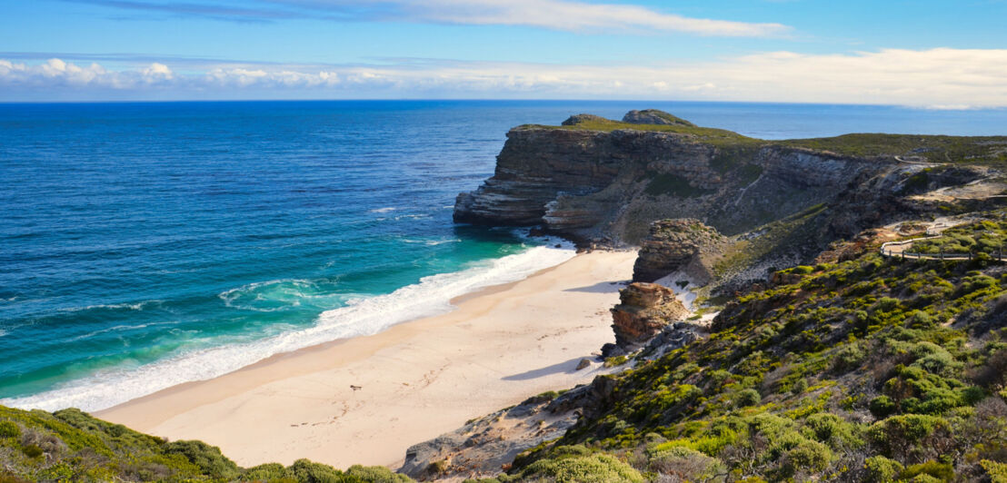 Sandstrand bei Kapstadt in einer Bucht an einer naturbelassenen, steilen Felsküste