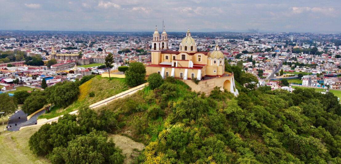 Eine Kirche auf einer mit Bäumen bewachsenen Pyramide vor Stadtpanorama