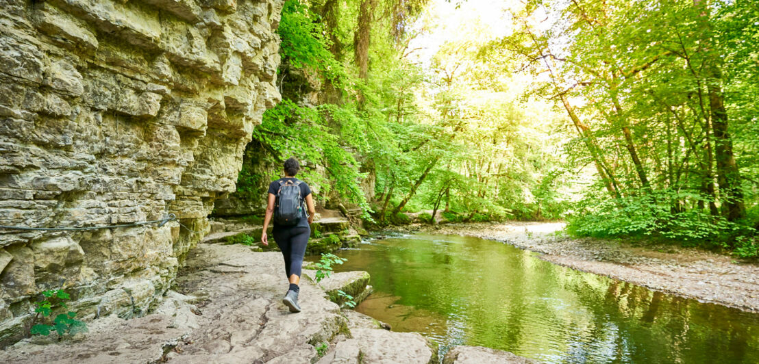 Eine Person mit Rucksack wandert an einem Fluss entlang