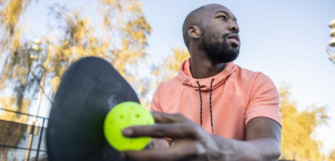 Nahaufnahme eines Spielers beim Aufschlag beim Pickleball auf einem Sportplatz unter freiem Himmel