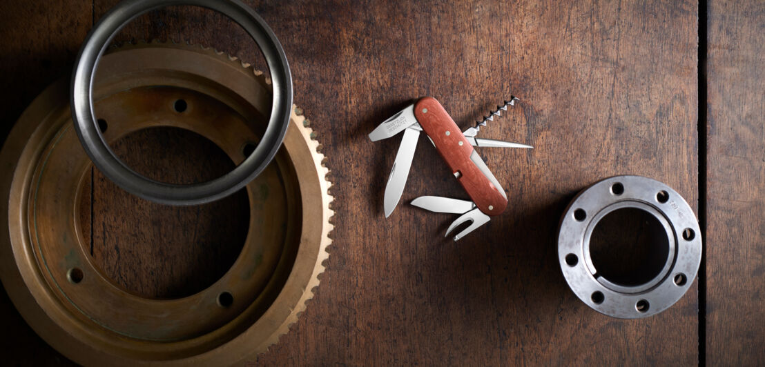 Ein aufgeklapptes Schweizer Taschenmesser mit Holzschale auf einem Holztisch