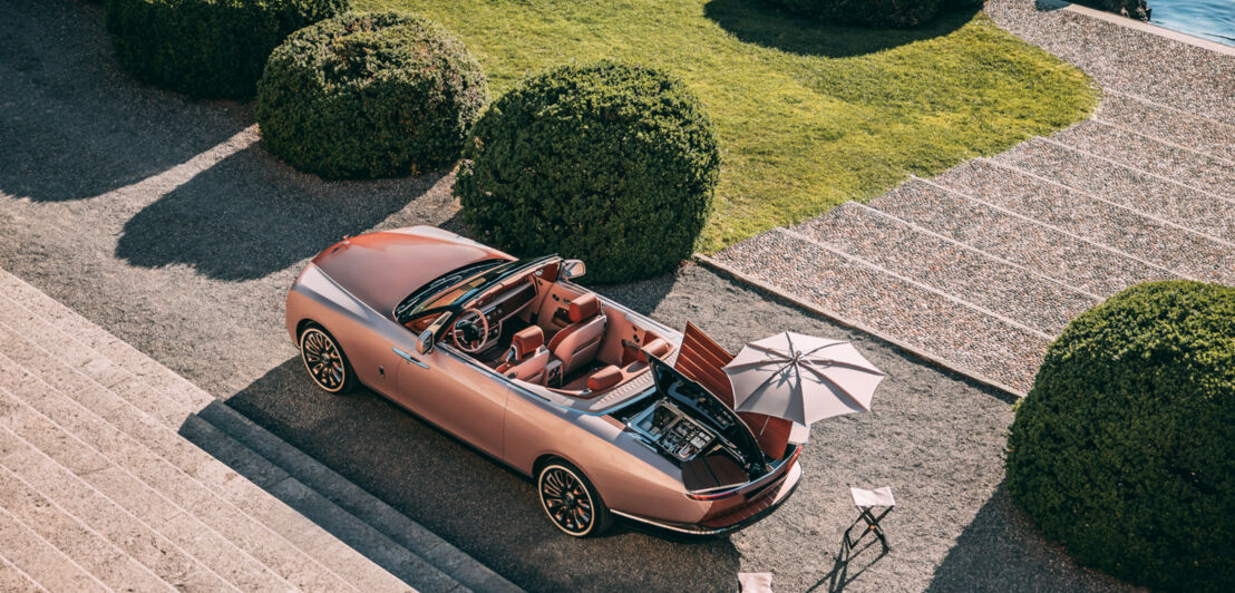 Luftaufnahme des Rolls-Royce Boat Tail in Roségold, das in einer prächtigen Parkanlage steht und einen Blick auf den Champagnerkühler gewährt