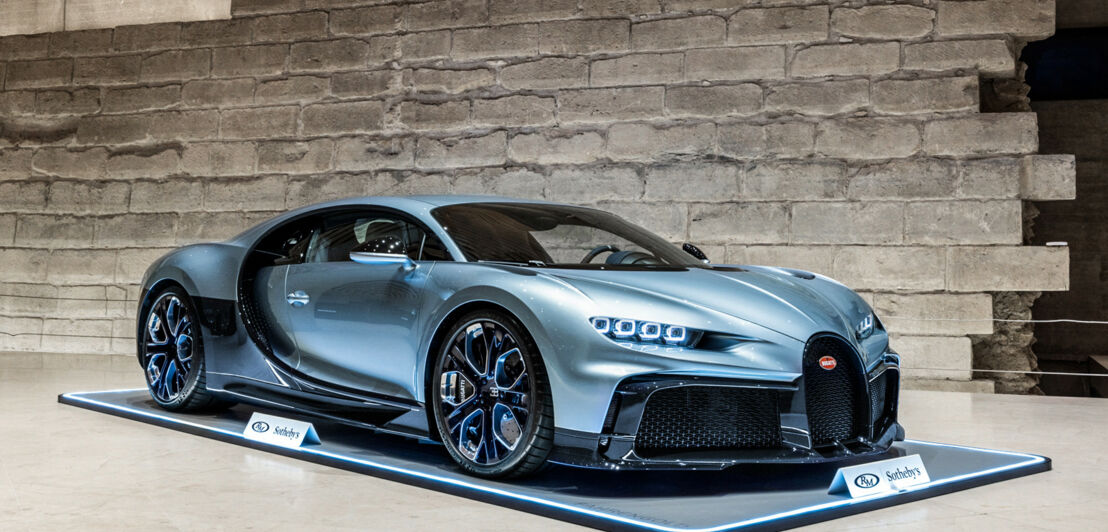 Ein blau-silberner Bugatti Chiron Profilée vor einer weißen Steinmauer ausgestellt