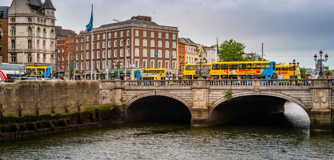 Über eine Brücke, die über den Liffey River führt, fahren mehrere Touristenbusse