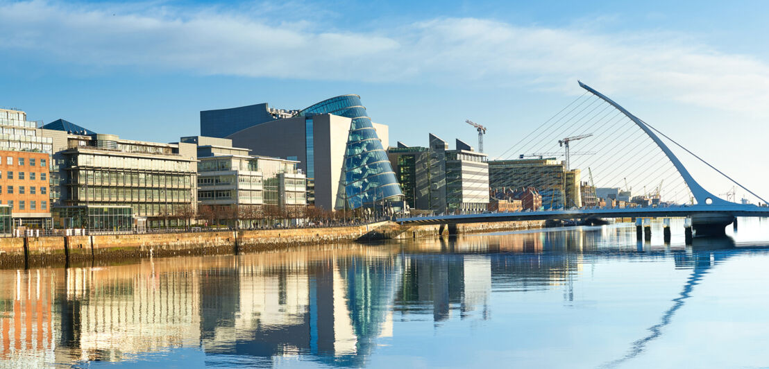 Moderne Gebäude sowie die Harfenbrücke über den Liffey River in Dublin an einem hellen, sonnigen Tag 