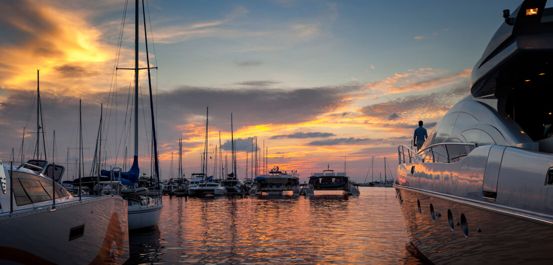 Mehrere Jachten, die bei Sonnenuntergang in einem kleinen Hafen stehen.