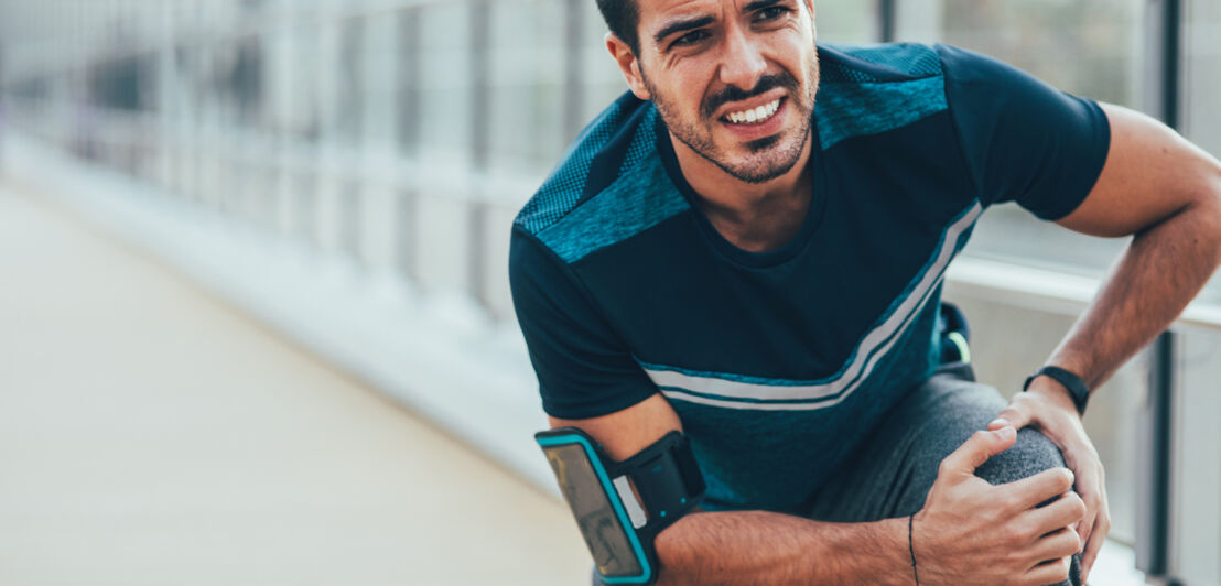 Ein Mann in Sportdress mit schmerzverzerrtem Gesicht, der sich sein linkes Knie hält