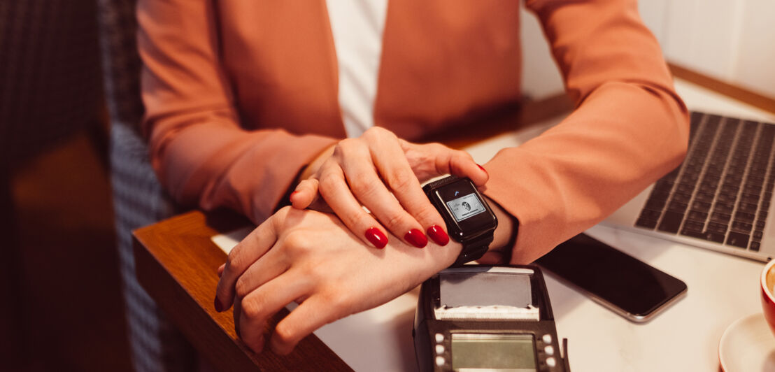 Eine Frau bezahlt mit einer American Express Kreditkarte via Apple Watch an einem Kartenlesegerät in einem Café