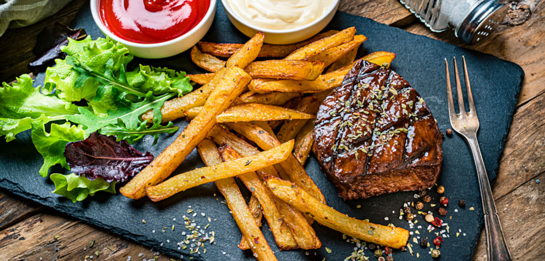 Steak, Pommes und Salat auf einer Granitplatte angerichtet, dazu eine Gabel