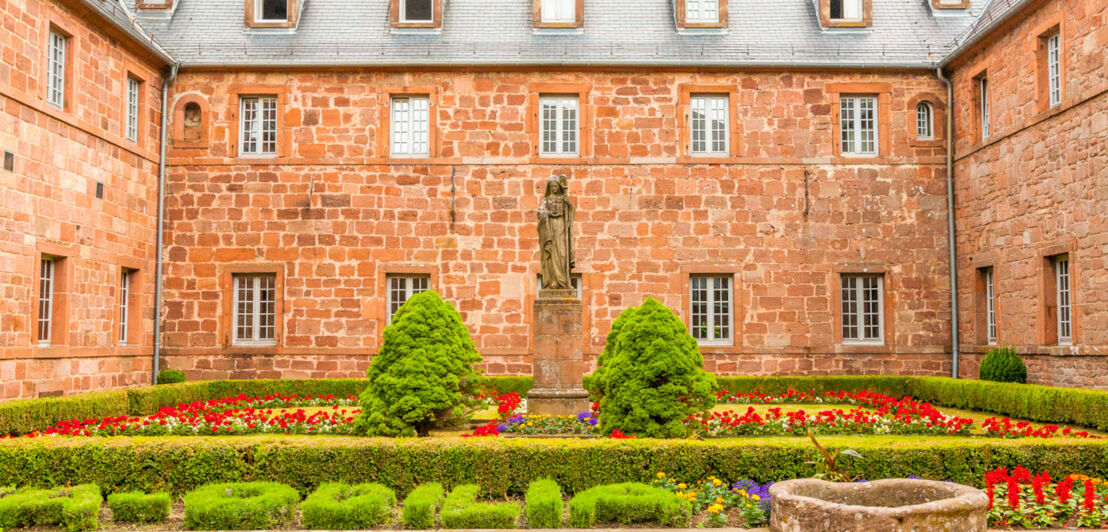 Blühender Klostergarten in einem Innenhof mit Sandsteinstatue in Frauengestalt im Zentrum