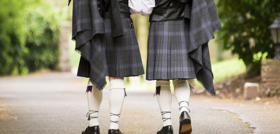 Zwei Männer von hinten in grau-blauem Kilt mit Tuch, Wollsocken und Schuhen