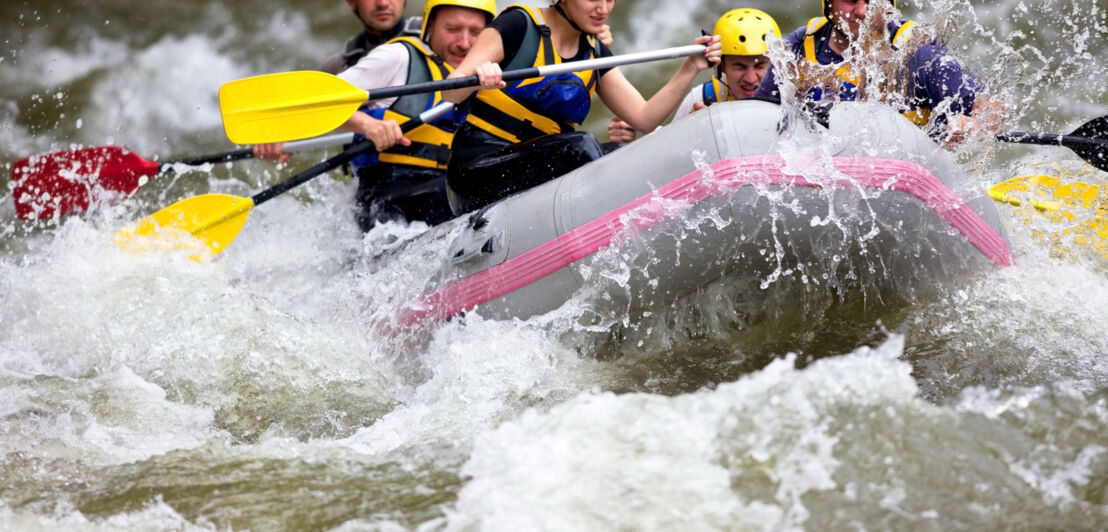 Eine Gruppe von Menschen mit gelben Helmen beim Wildwasser-Rafting auf einem Fluss