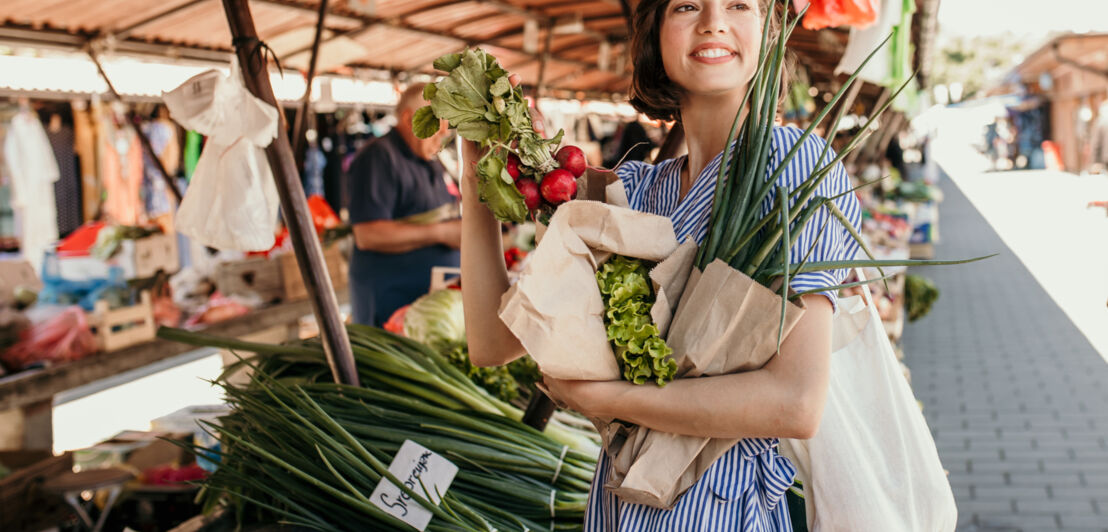 Eine junge Frau kauft auf einem Wochenmarkt regionales Gemüse in Papiertüten ein