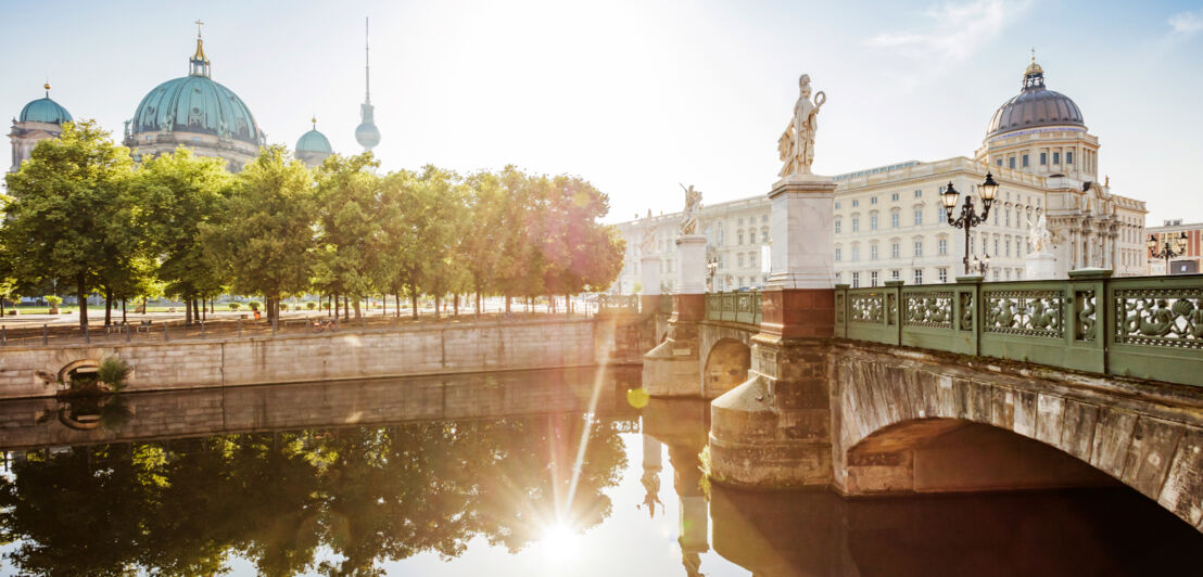 Berliner Dom und Humboldt Forum mit Brücke und Wasser im Vordergrund bei Sonnenschein.